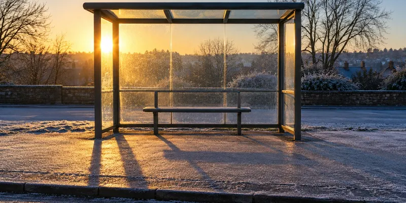 An empty glass bus shelter on a frosty pavement just after sunrise.