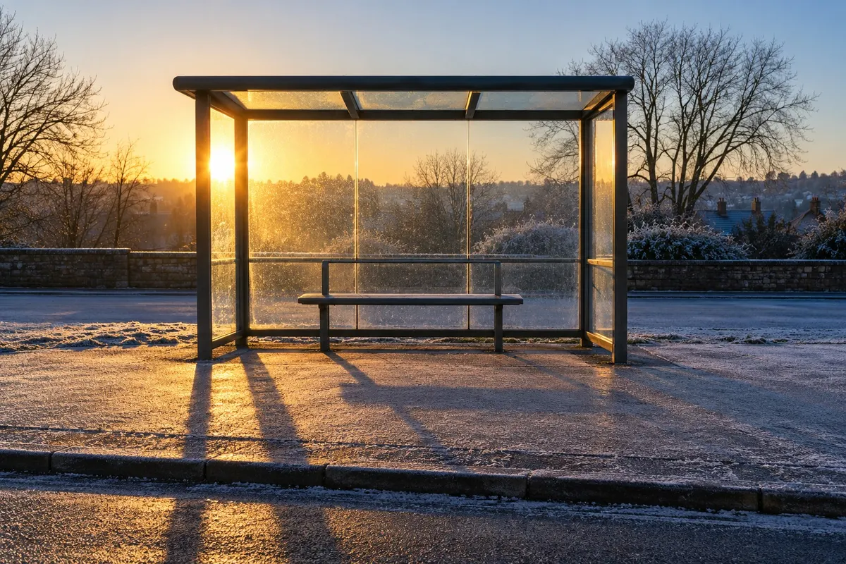 An empty glass bus shelter on a frosty pavement just after sunrise.